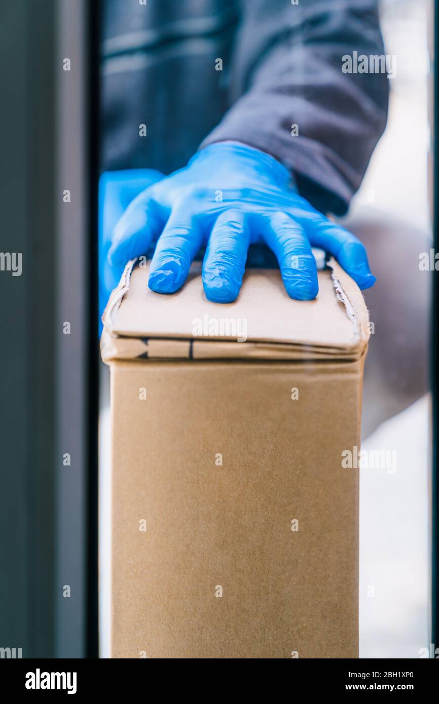 Livreur laissant un colis à la porte du client comme mesure de protection contre le coronavirus. Homme de livraison portant des gants en latex bleu. Livrer Banque D'Images
