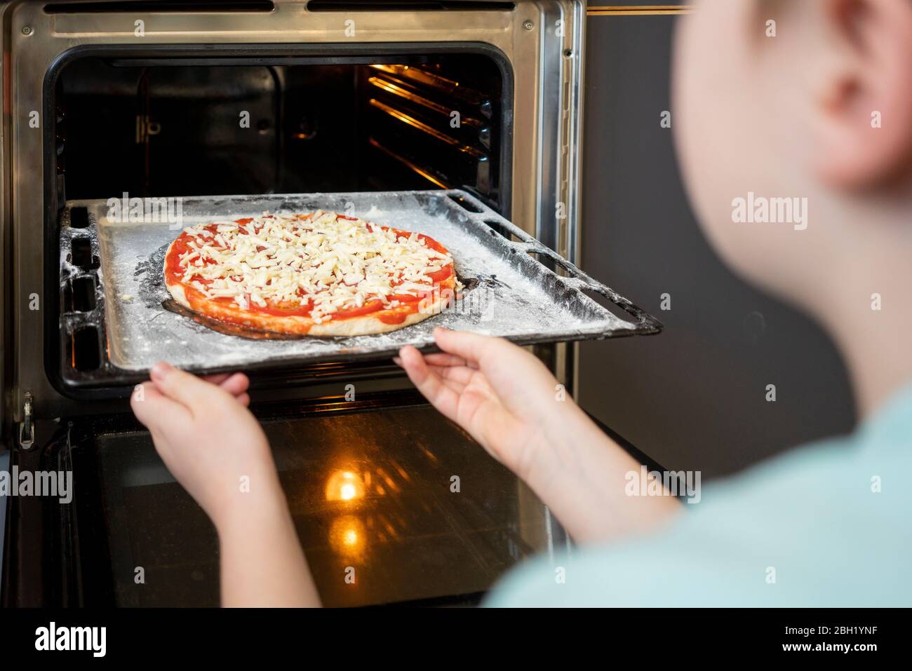 Vue rognée du petit garçon poussant la plaque de cuisson avec pizza crue dans le four Banque D'Images