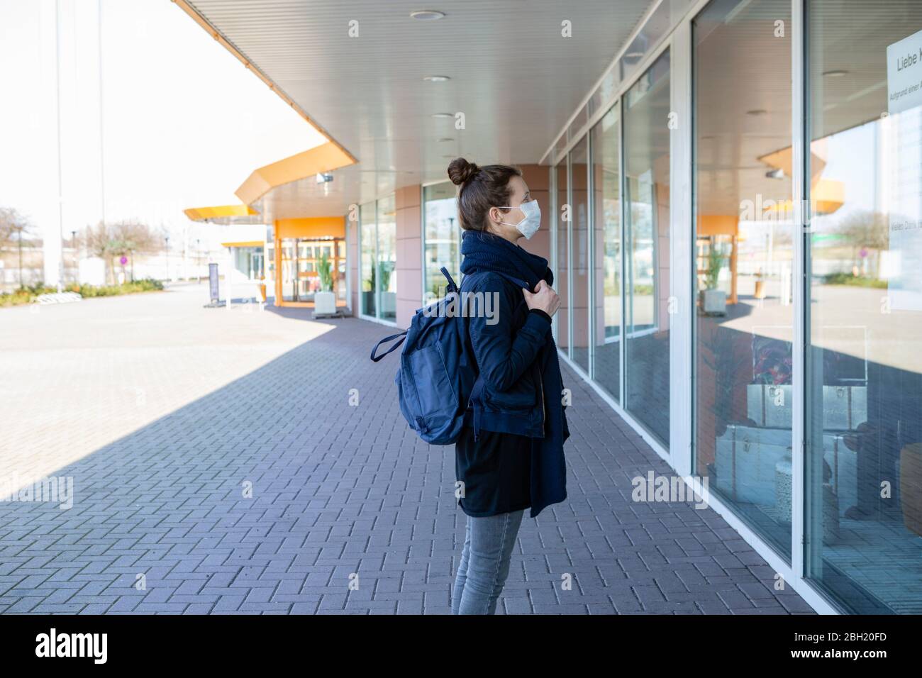 Femme avec masque debout devant une fenêtre d'exposition de centre commercial fermé Banque D'Images