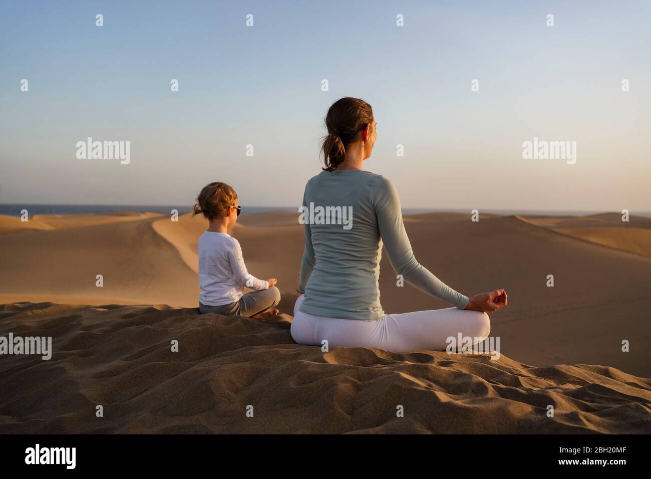 Mère et fille pratiquant le yoga dans les dunes de sable au coucher du soleil, Gran Canaria, Espagne Banque D'Images