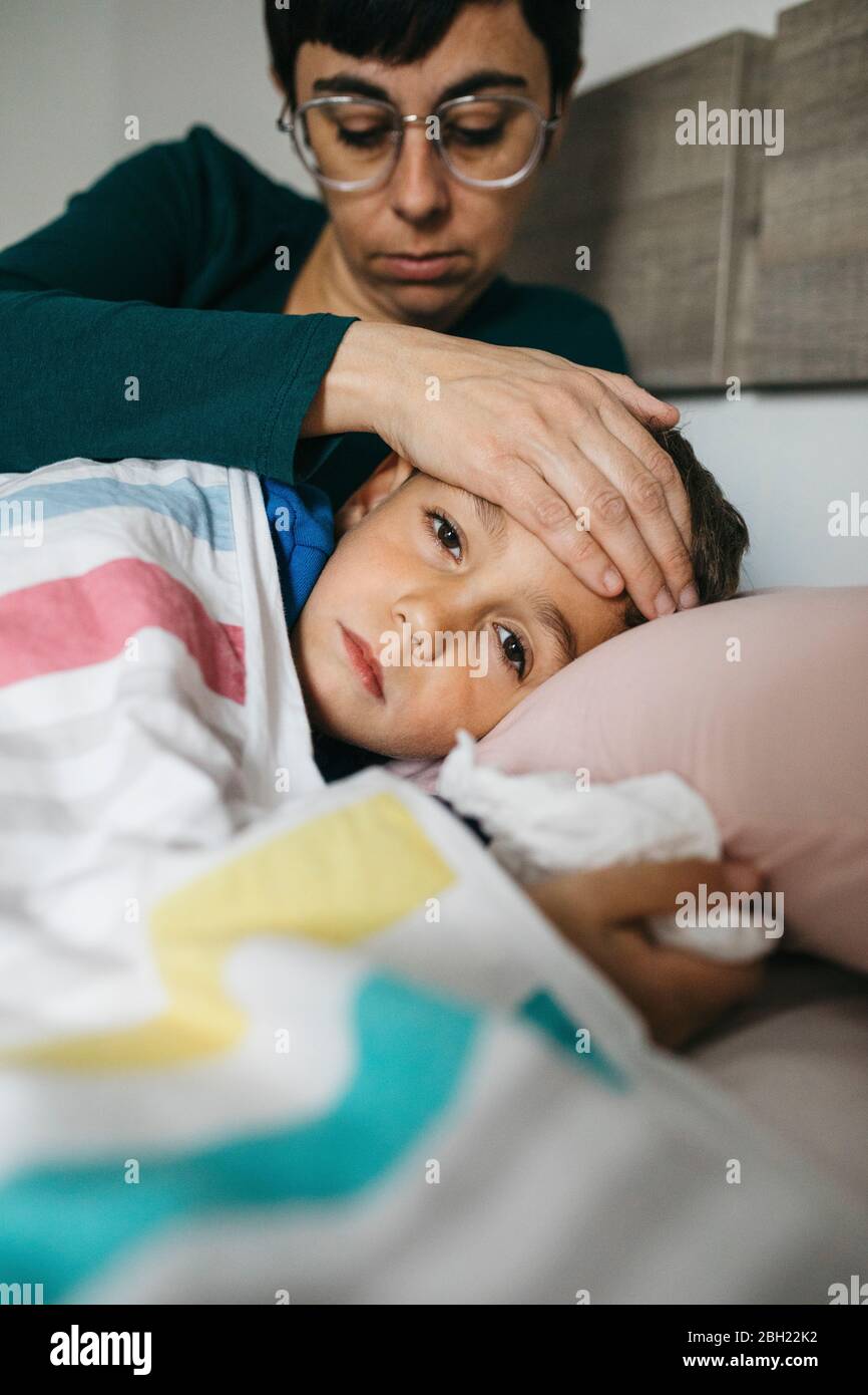 Portrait d'un garçon malade allongé dans le lit alors que sa mère touche son front Banque D'Images