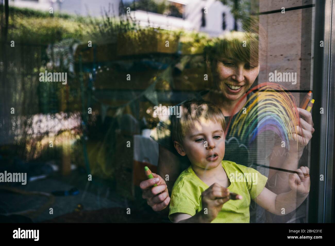 Mère et petit fils à la maison dessinant arc-en-ciel sur la fenêtre Banque D'Images