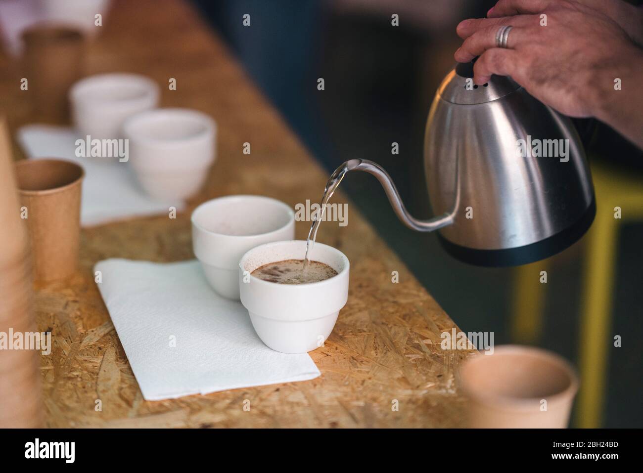 Gros plan d'un homme travaillant dans une maîtrise de café versant de l'eau chaude dans des tasses de café Banque D'Images Gros plan d'un homme travaillant dans une maîtrise de café versant de l'eau chaude dans des tasses de café Banque D'Images