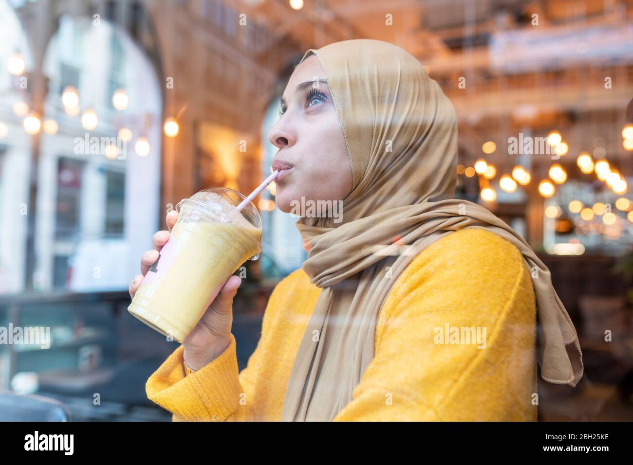 Jeune femme portant le hijab buvant du smoothie dans un café Banque D'Images