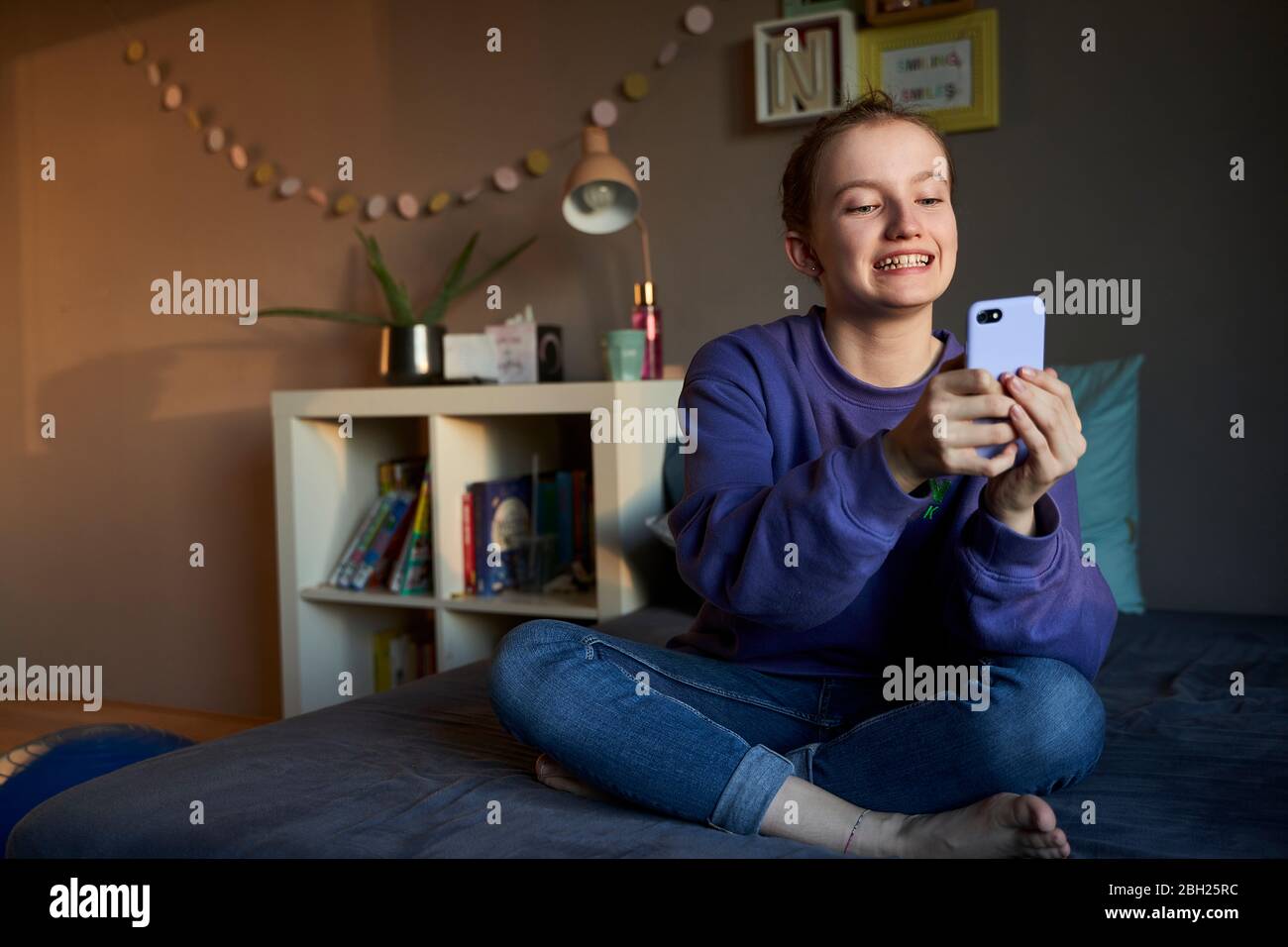 Portrait de la fille à sourire assis sur le lit prenant selfie avec un smartphone Banque D'Images
