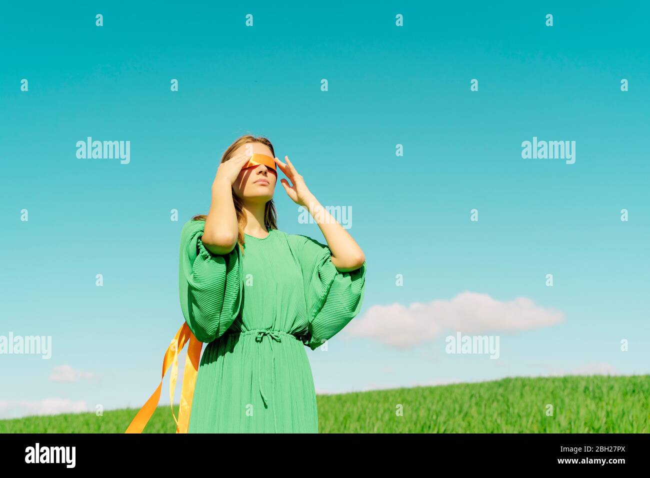 Une jeune femme aux yeux bandés portant une robe verte debout dans un champ Banque D'Images