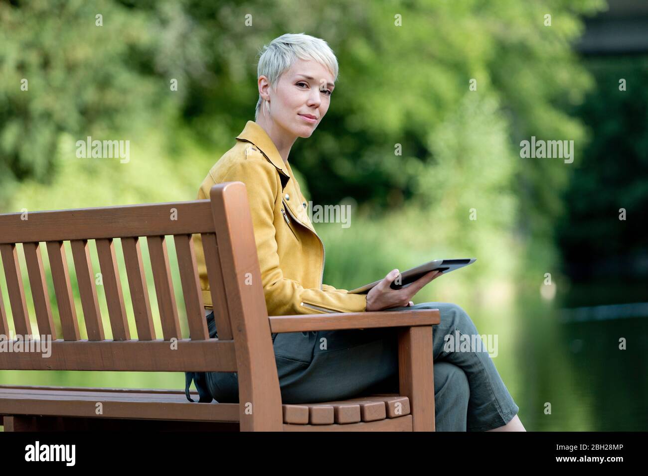 Portrait d'une tablette numérique de femme assise sur un banc en bois dans un parc Banque D'Images