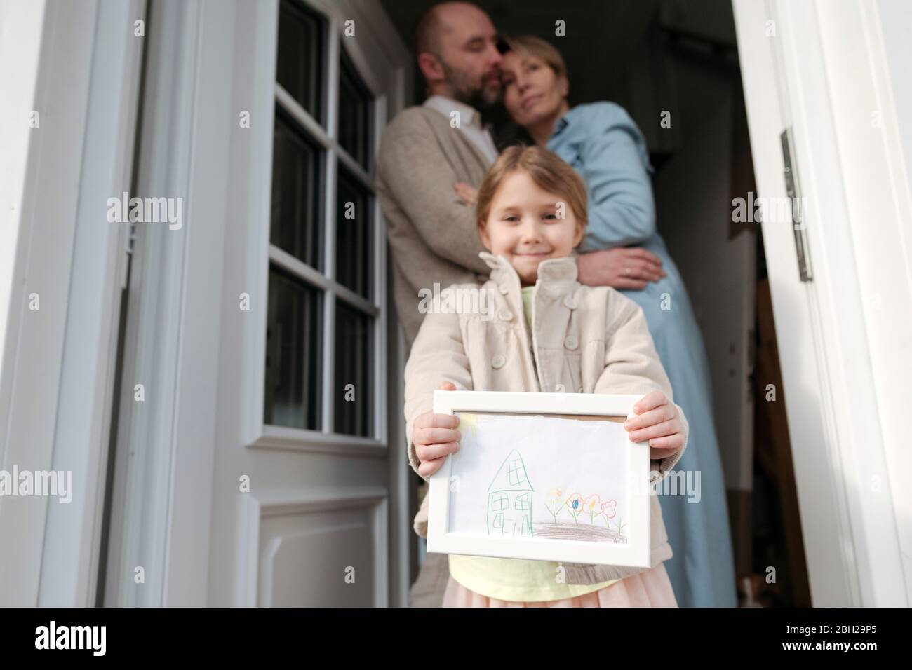 Bonne petite fille avec dessin de sa maison et parents embrassant derrière elle Banque D'Images