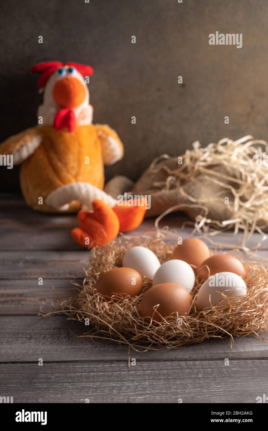 Les œufs de poulet brun et blanc nichent dans un nid de paille sur fond de bois. À côté d'un jouet de poulet. Orientation verticale Banque D'Images