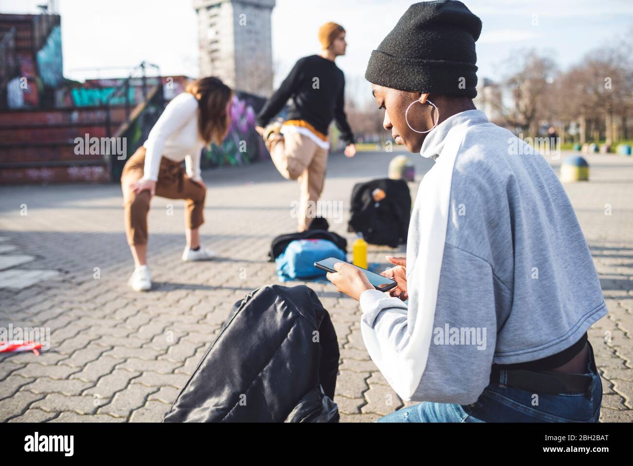 De jeunes danseurs se répètent dans un parc de skare, une jeune femme utilisant un smartphone Banque D'Images