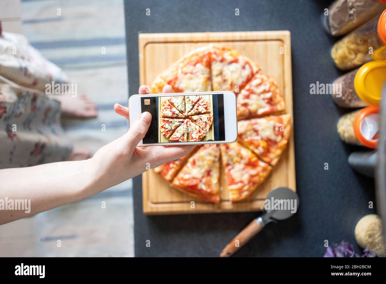 Vue rognée d'une femme prenant des photos de pizza maison avec un smartphone Banque D'Images