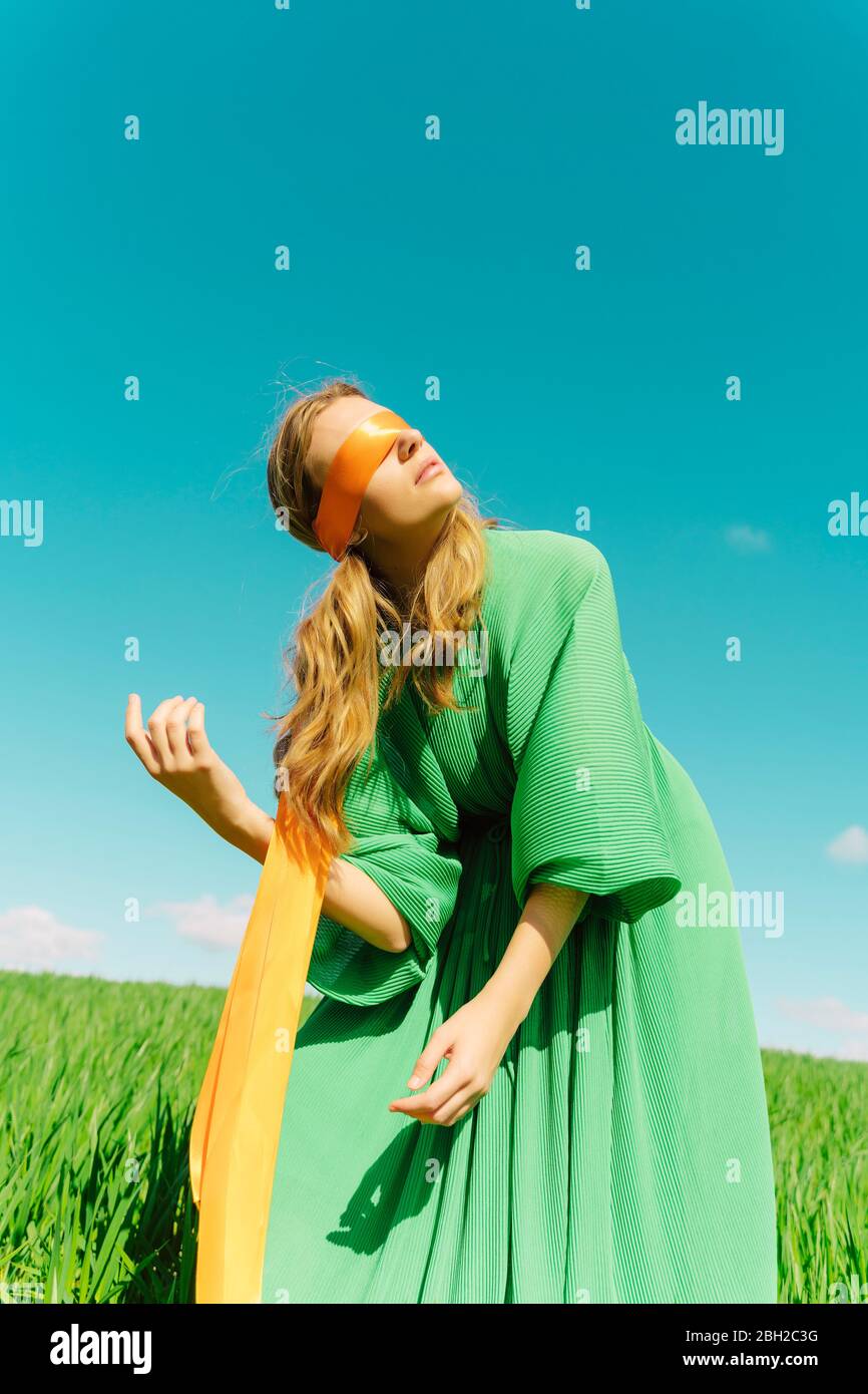 Une jeune femme aux yeux bandés portant une robe verte debout dans un champ Banque D'Images