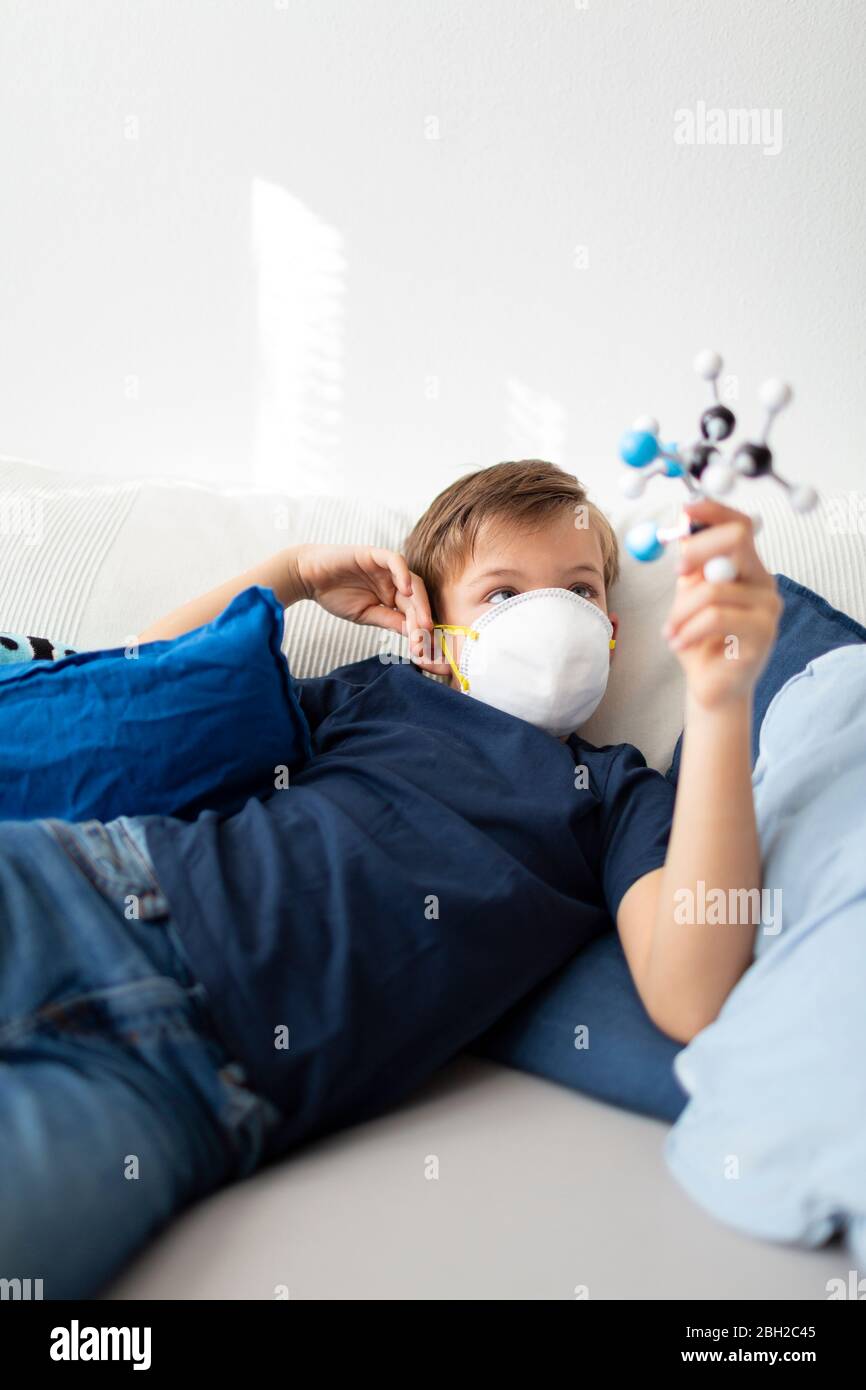 Garçon avec masque est dans sa chambre jouant avec un modèle moléculaire à la maison pendant la crise corona Banque D'Images