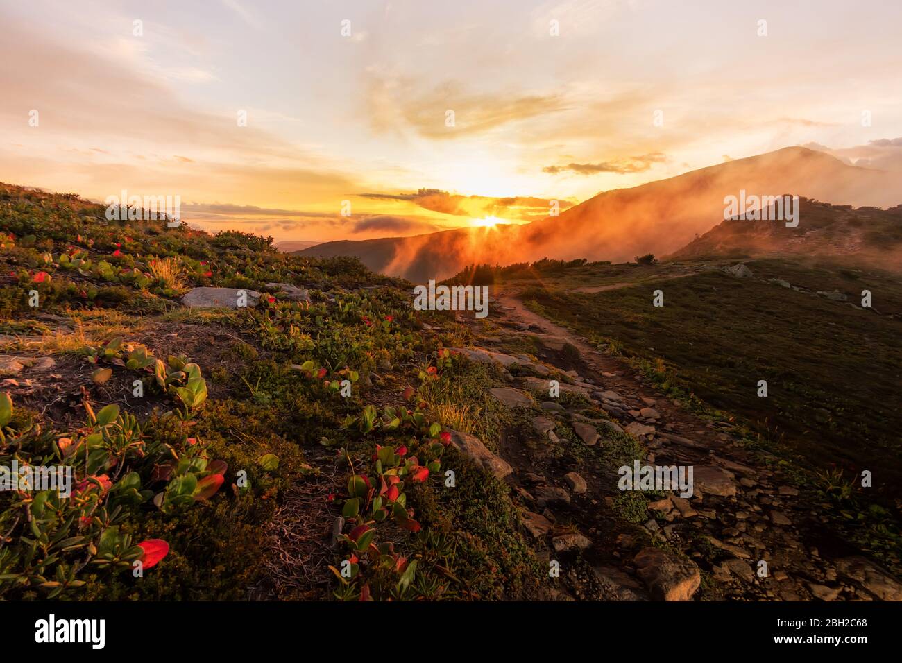 Paysage de montagne lever de soleil rouge-orange dans le brouillard et les nuages, à savoir de la piste à la vallée. Banque D'Images