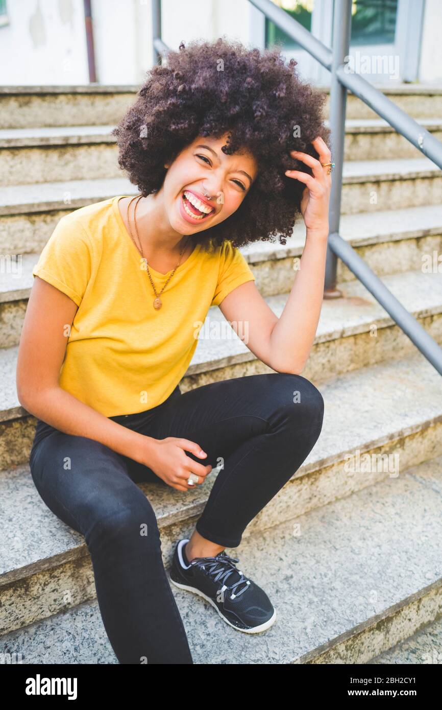 Portrait de jeune femme en train de rire assise dans les escaliers à l'extérieur Banque D'Images