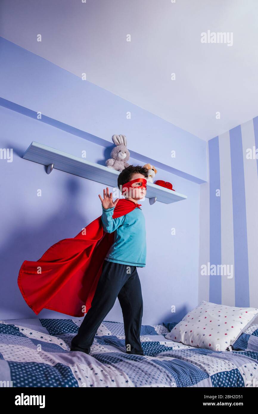 Petit garçon jouant super héros, debout sur son lit Banque D'Images