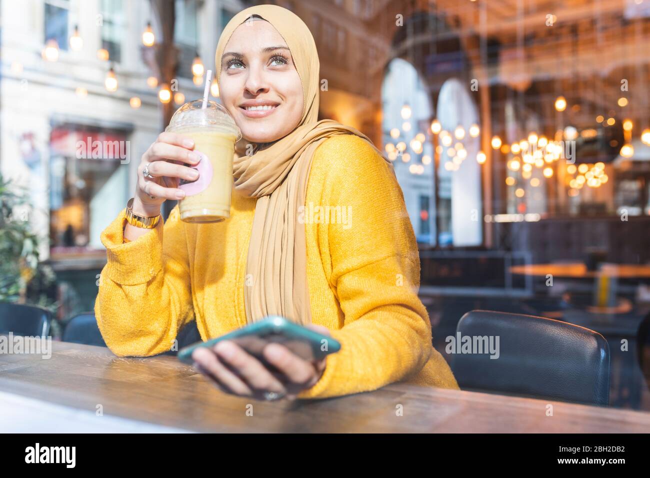 Portrait d'une jeune femme avec smoothie et smartphone dans un café Banque D'Images