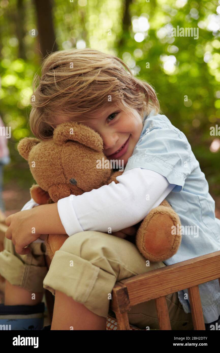 Portrait d'un garçon qui embrasse un ours en peluche en forêt Banque D'Images
