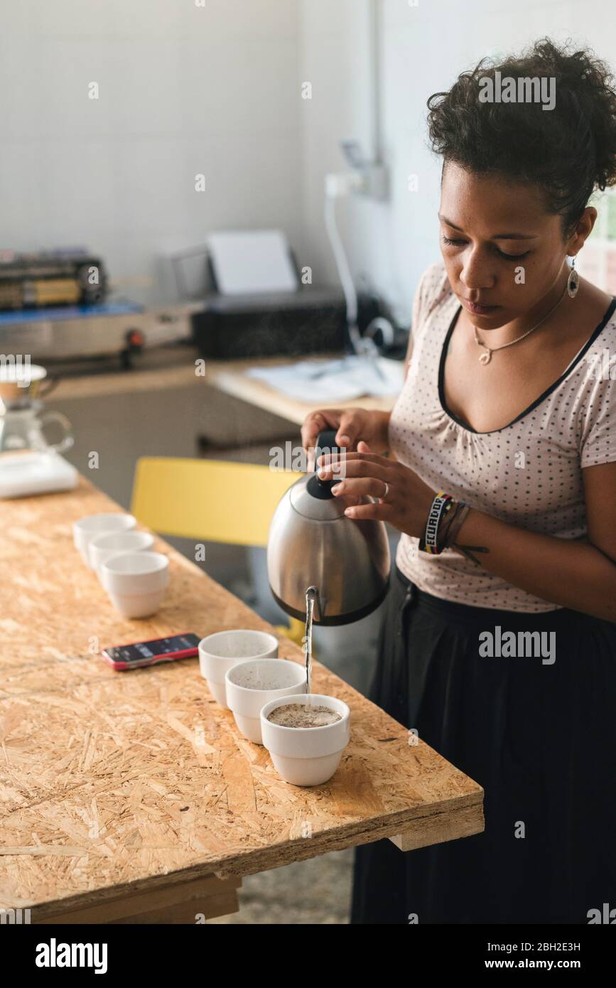 Femme travaillant dans une maîtrise de café versant de l'eau chaude dans des tasses de café Banque D'Images