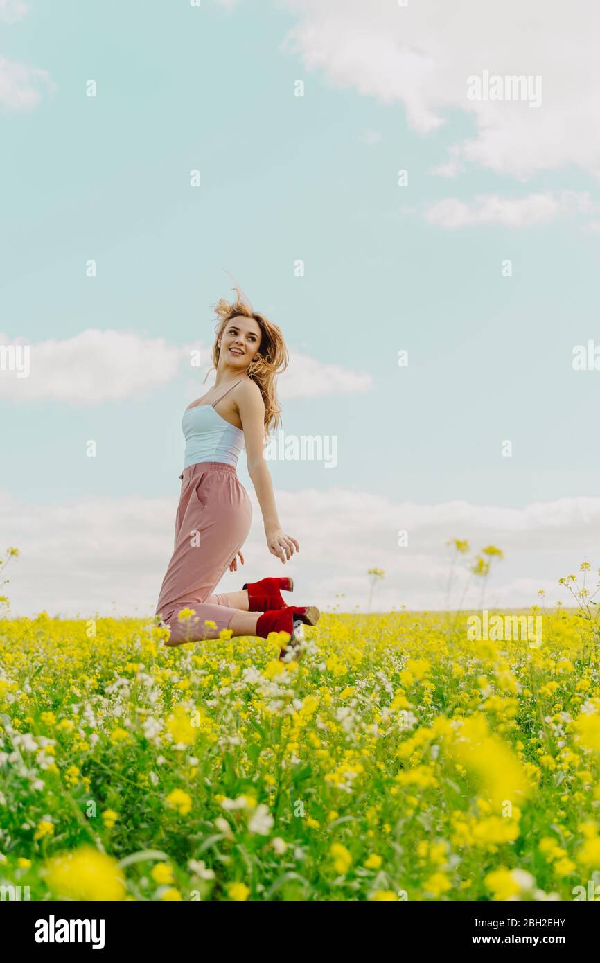 Bonne jeune femme sautant dans un pré de fleurs au printemps Banque D'Images