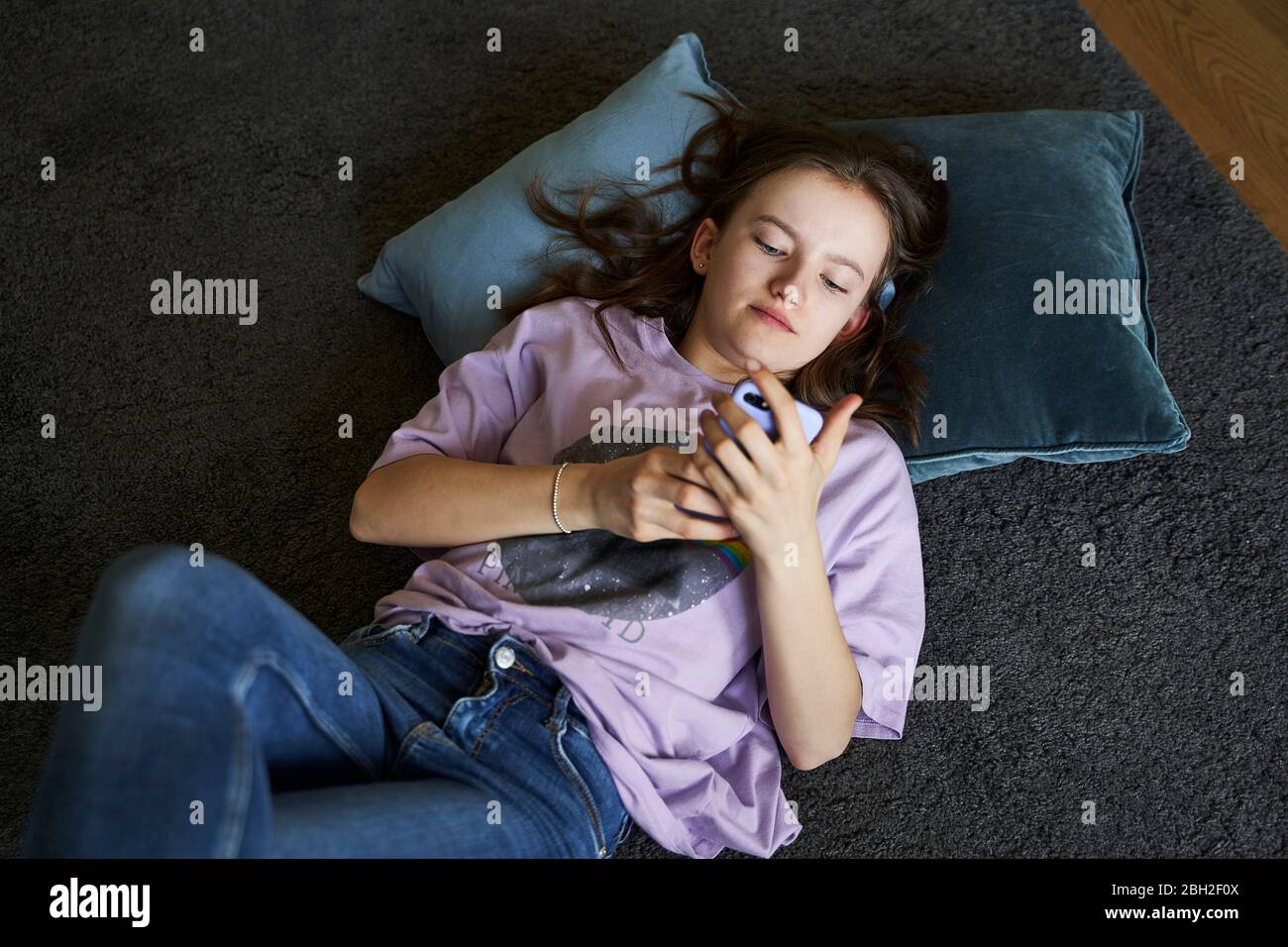 Portrait d'une fille qui se trouve sur le sol à la maison et qui regarde un smartphone Banque D'Images