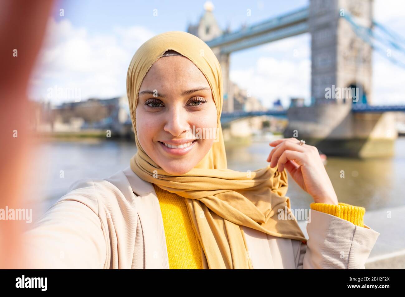 Portrait d'une jeune femme souriante prenant le selfie devant Tower Bridge, Londres, Royaume-Uni Banque D'Images