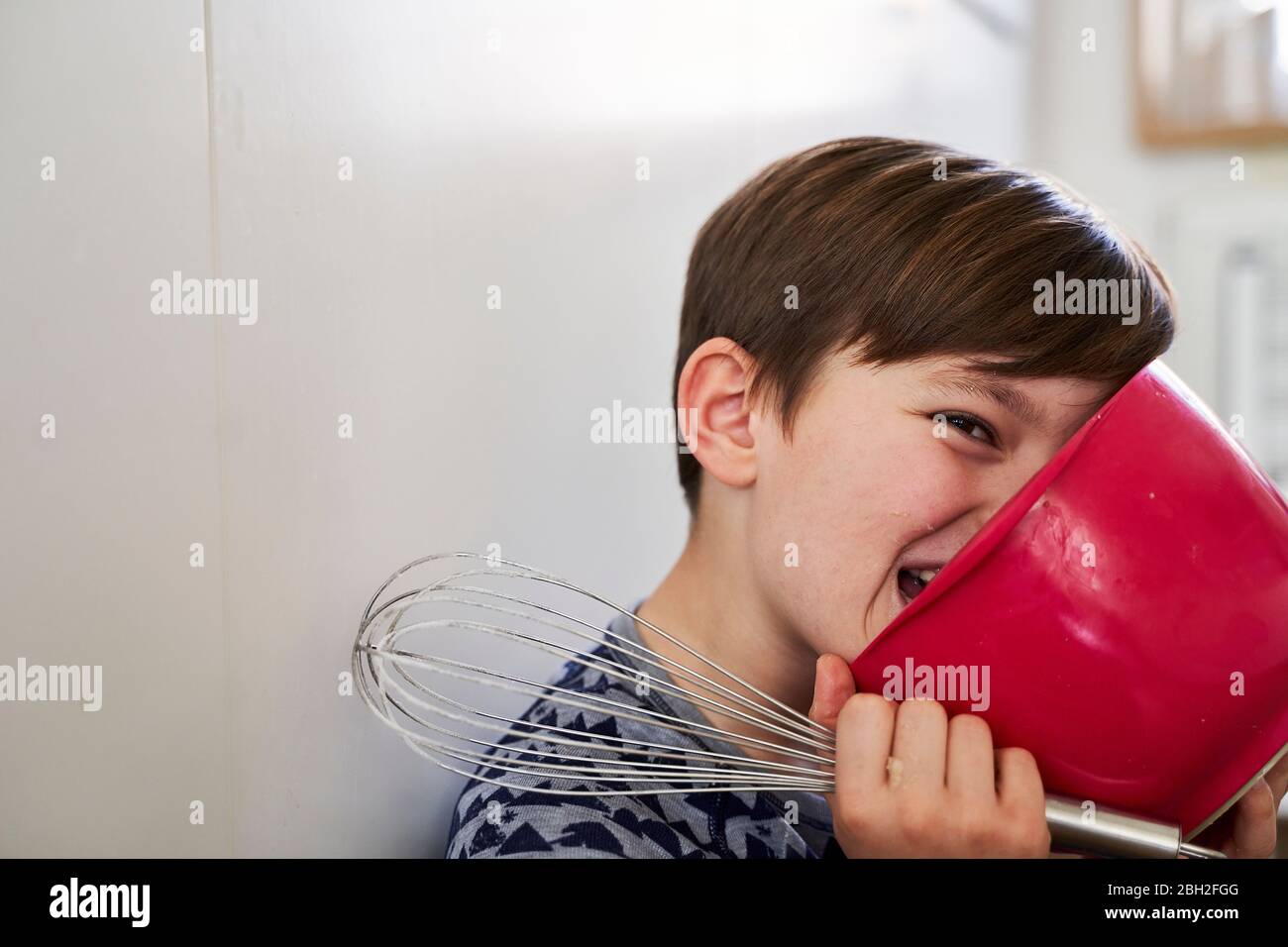 Portrait d'un garçon avec bol mélangeur rouge et batteur à œufs dans la cuisine Banque D'Images