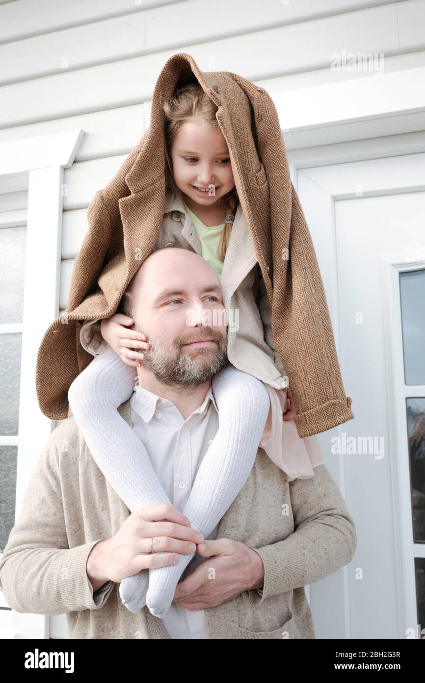 Portrait du père avec sa fille sur ses épaules devant leur maison Banque D'Images
