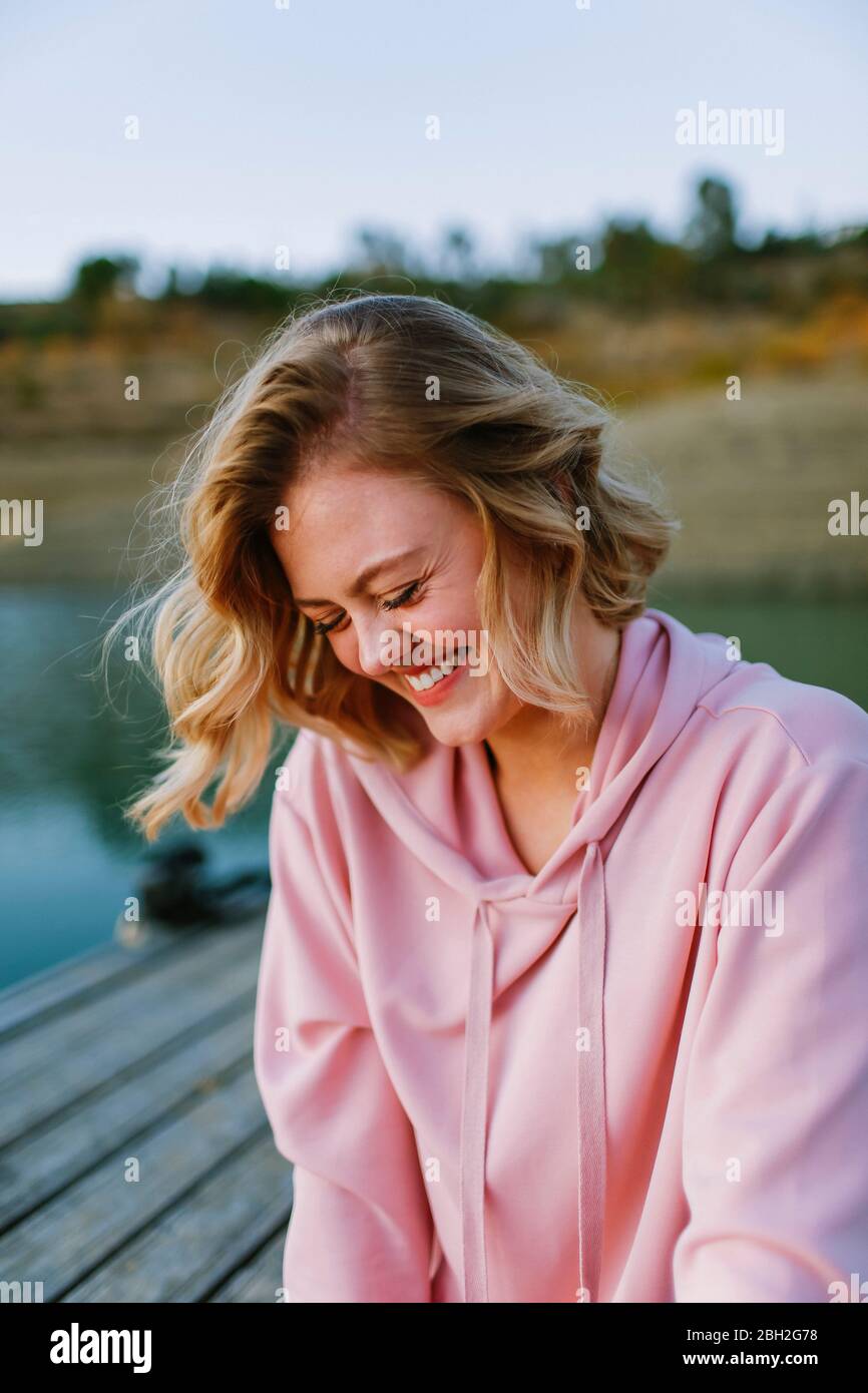 Portrait d'une jeune femme en train de rire portant un pull à capuche rose sur la jetée Banque D'Images