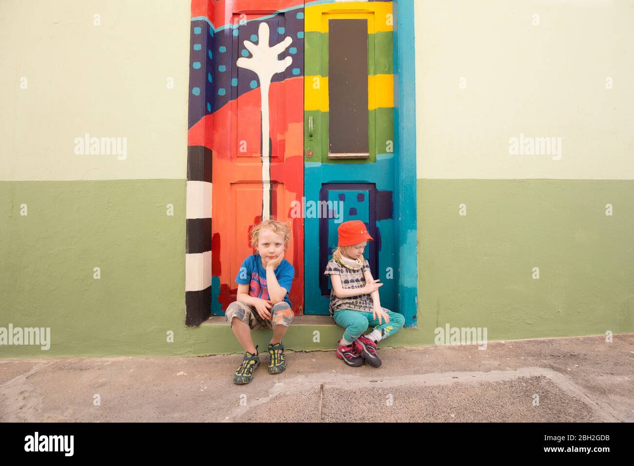 Portrait du garçon et de sa petite sœur assis ensemble sur la marche devant la porte d'entrée peinte en couleur Banque D'Images