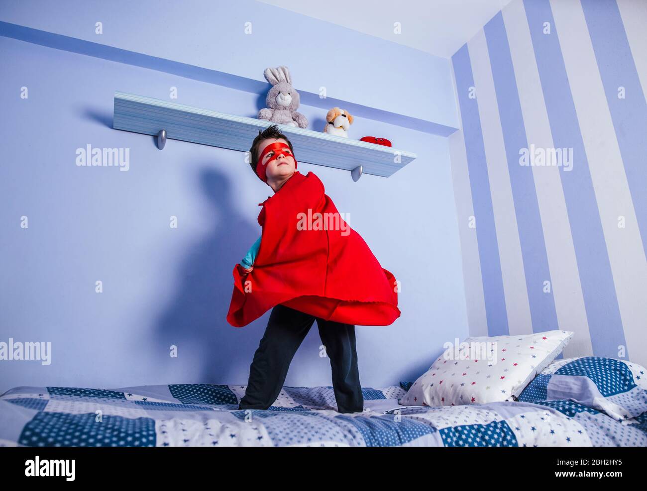 Petit garçon jouant super héros, debout sur son lit Banque D'Images