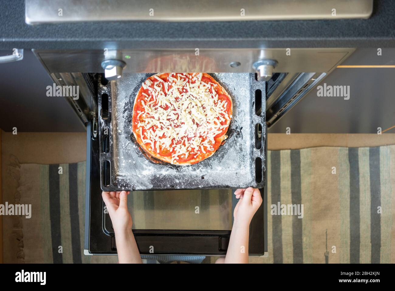 Mains de garçon tenant une plaque de cuisson avec une pizza maison crue Banque D'Images