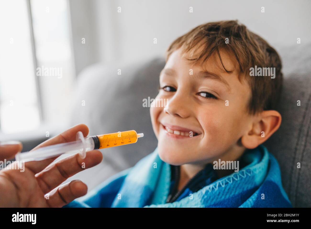 Portrait de sourire un garçon malade assis sur un canapé pendant que sa mère lui donne des médicaments Banque D'Images