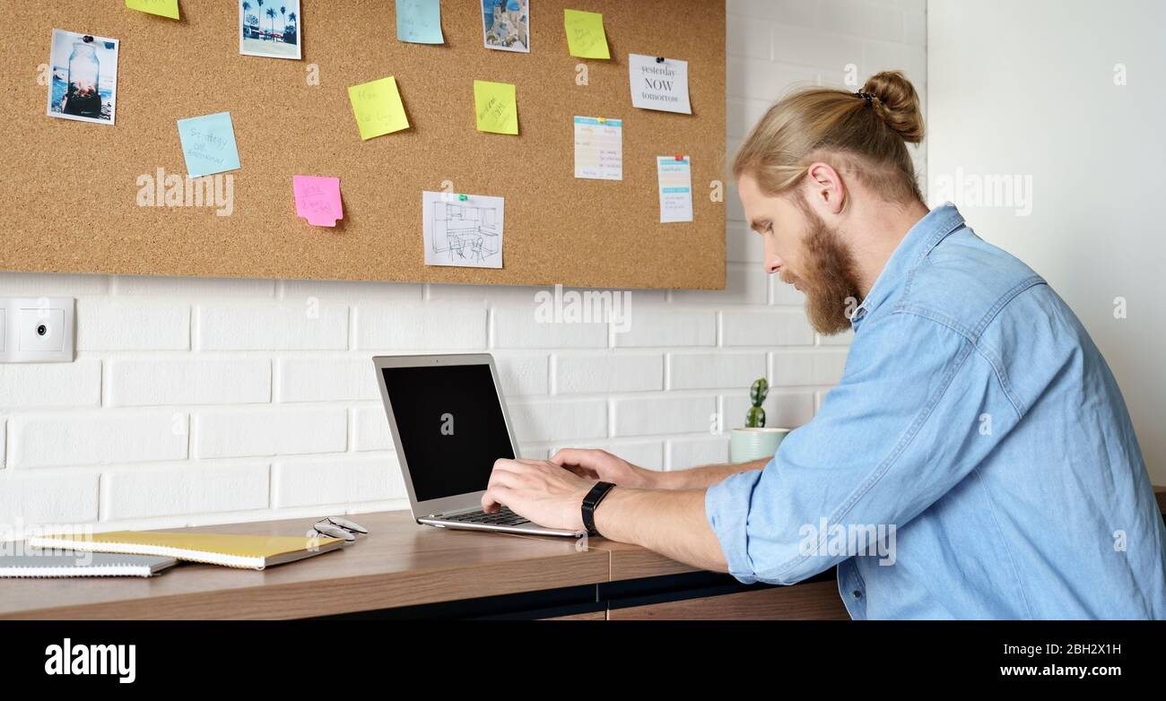 Homme sérieux utilisant un ordinateur portable travaillant ou étudiant à la maison assis au bureau. Banque D'Images