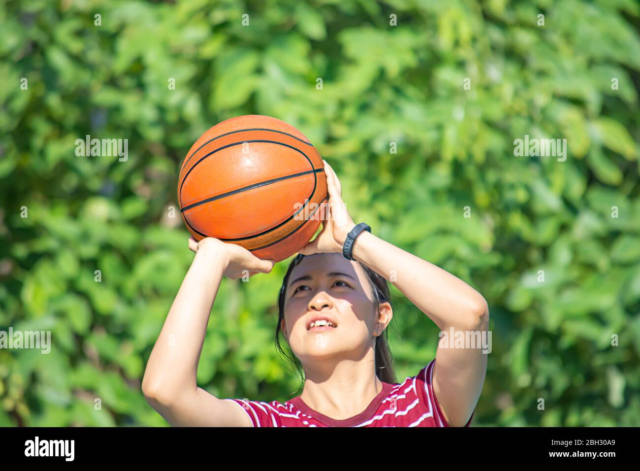 Basket-ball en cuir dans la main d'une femme portant une montre fond flou arbre en parc. Banque D'Images