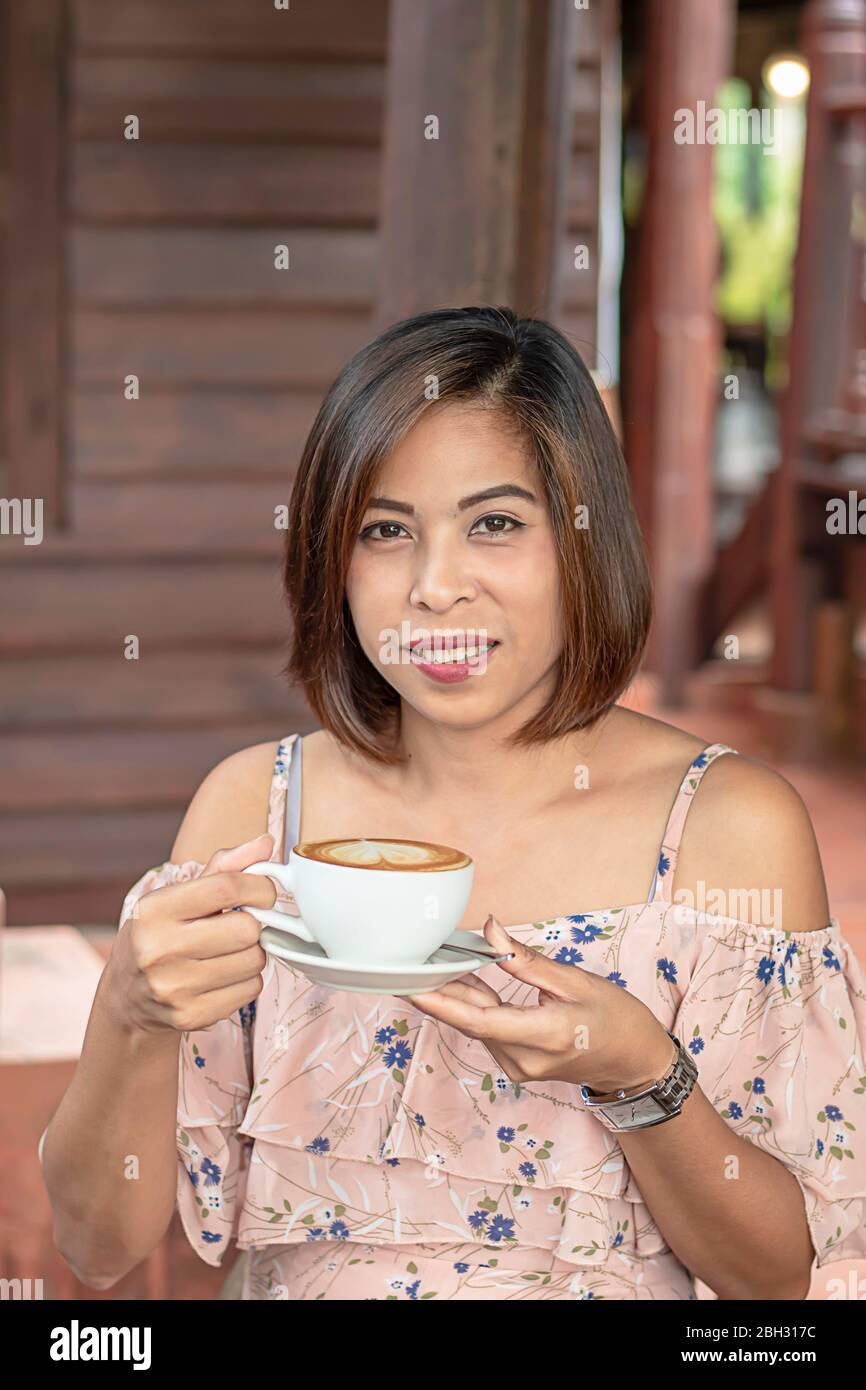 Part Asian woman holding Hot coffee Espresso surmonté d'un lait en forme de cœur en verre blanc. Banque D'Images