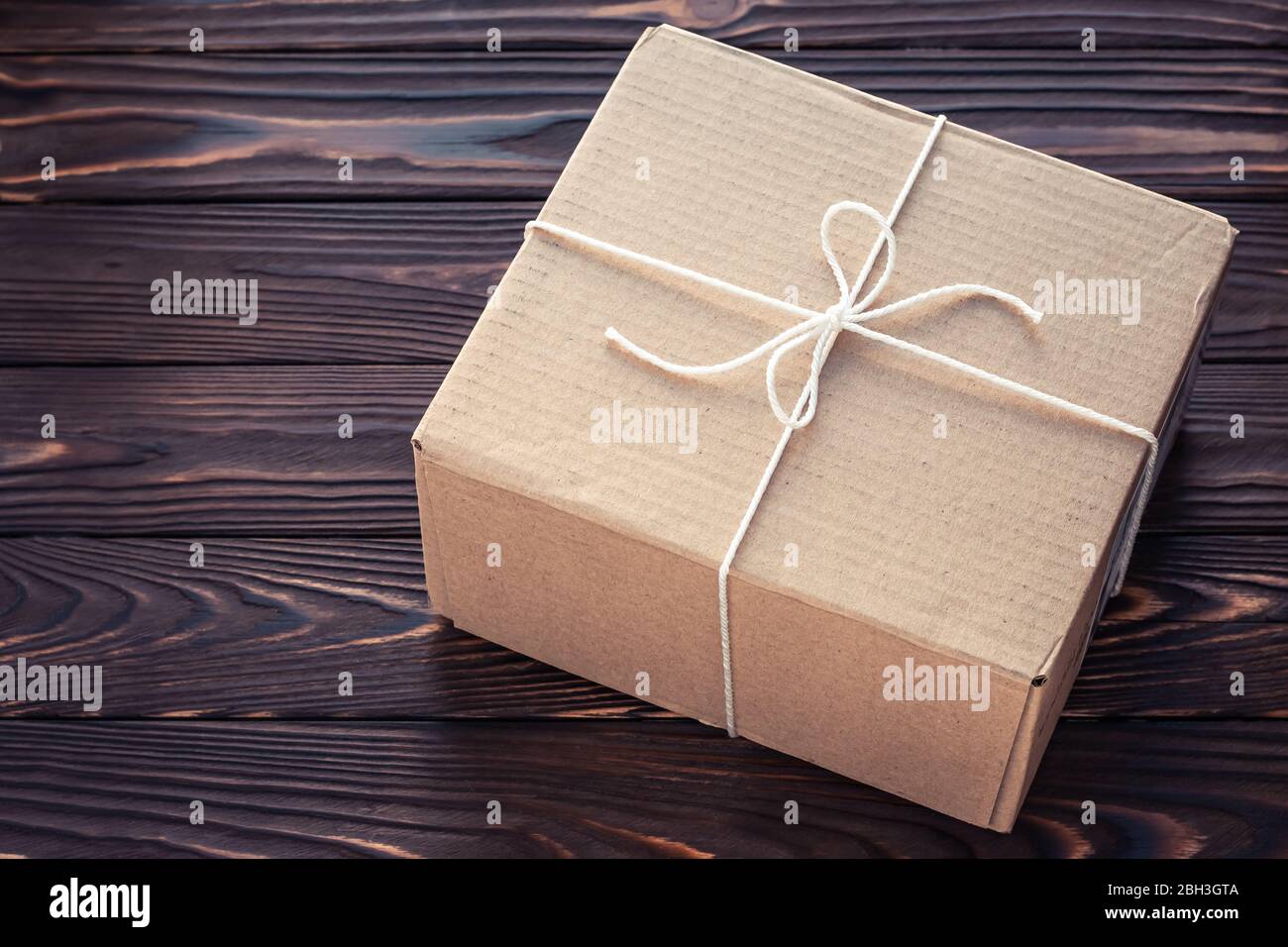 Boîte en carton marron attachée de fil sur des panneaux en bois sombre. Concept de service de livraison de colis Banque D'Images
