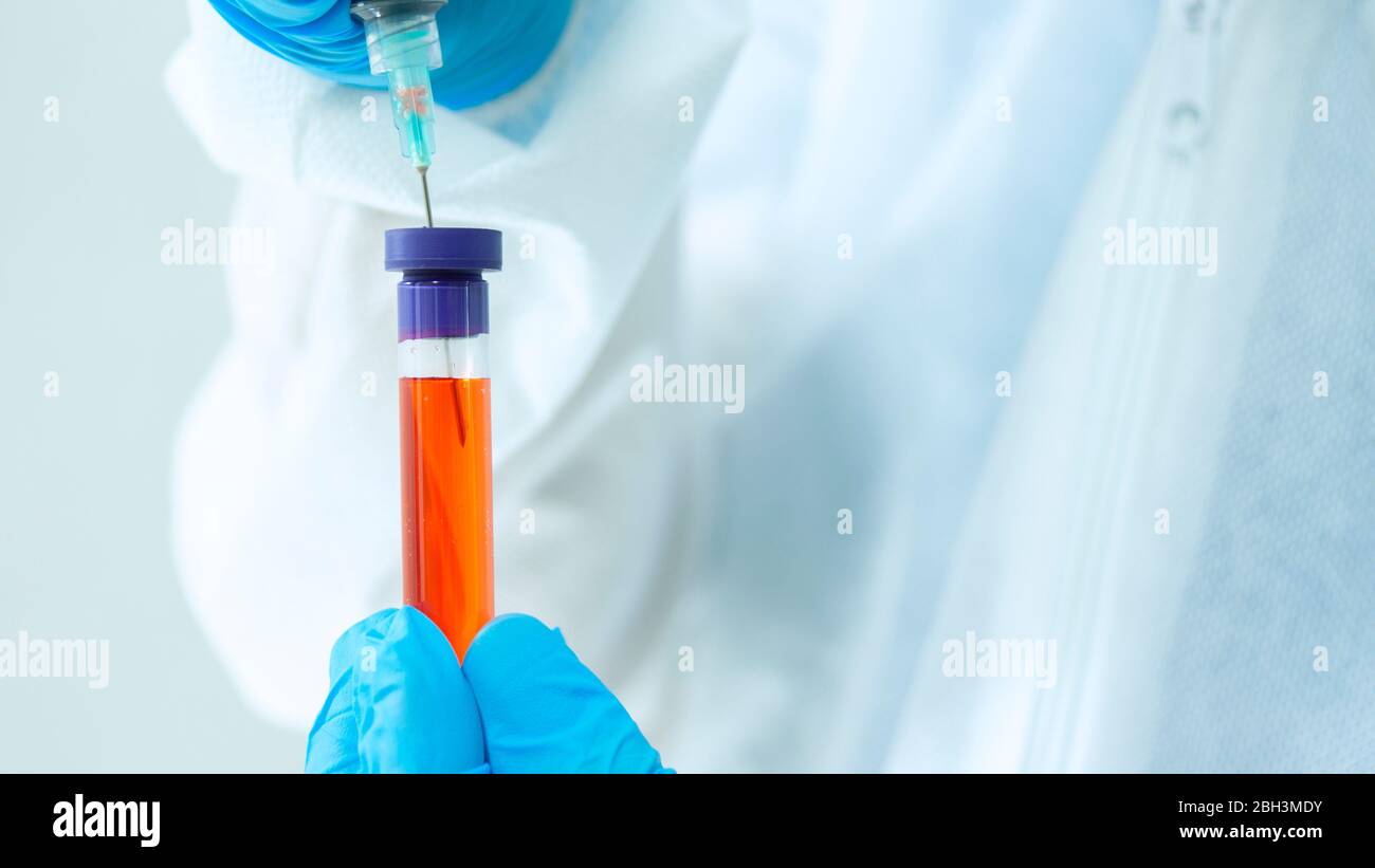 Vue rapprochée du médecin dans un costume de bioprotection et des gants bleus prenant un échantillon sanguin dans un tube à essai avec une seringue sur fond blanc Banque D'Images