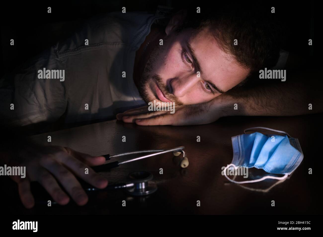 Un médecin épuisé se reposant sur la table la nuit avec l'éclairage de l'écran du téléphone portable, les masques de collier et la bouteille de désinfectant pour les mains de gel alcoho Banque D'Images