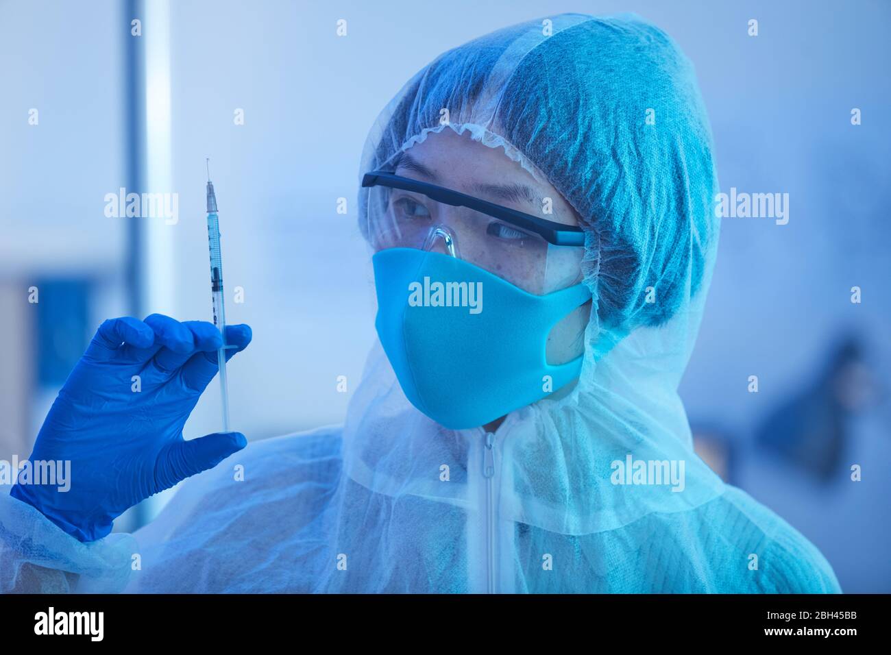 Médecin féminin en costume de protection tenant la seringue avec la médecine dans sa main pendant que travailler à l'hôpital Banque D'Images