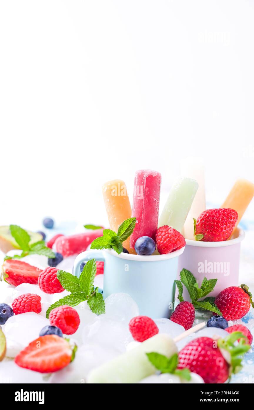 Des papoles de fruits entiers et sains avec des fraises Berries Kiwi sur fond clair, avec un décor de glace, de menthe. Une délicieuse glace aux fruits dans le mug. Espace de copie. Banque D'Images