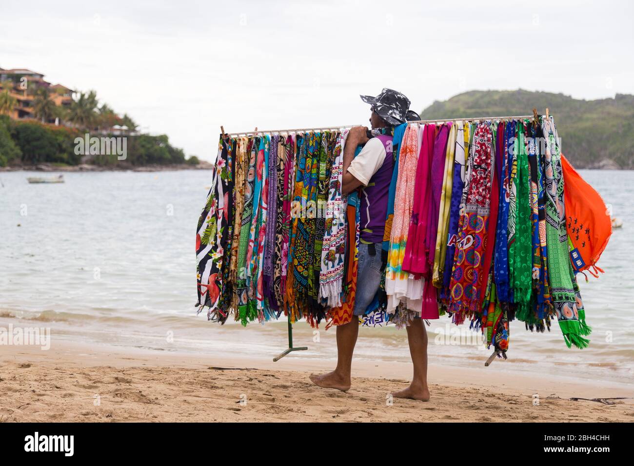 Vendeur de plage typique brésilienne marchant sur la plage et portant pour la vente des robes de plusieurs couleurs. FERRADURA BEACH, BUZIOS, BRÉSIL. Banque D'Images