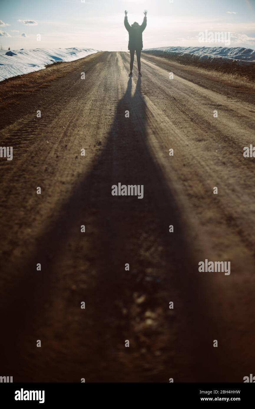Une femme courageuse sautant pour la joie au milieu d'une route de terre en hiver Banque D'Images