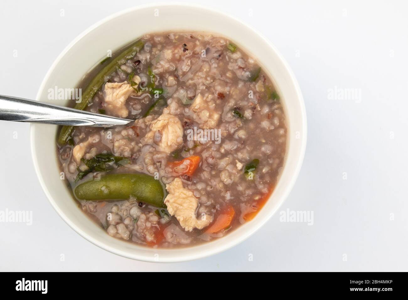 Délicieux porridge de riz brun maison avec peu de tranches de poulet, de carottes et de légumes isolés sur fond blanc. Banque D'Images