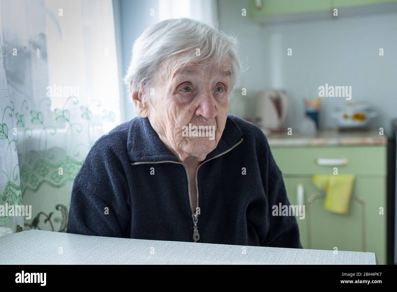 Portrait de la vieille femme solitaire assis dans la cuisine près de la fenêtre dans sa maison. Banque D'Images
