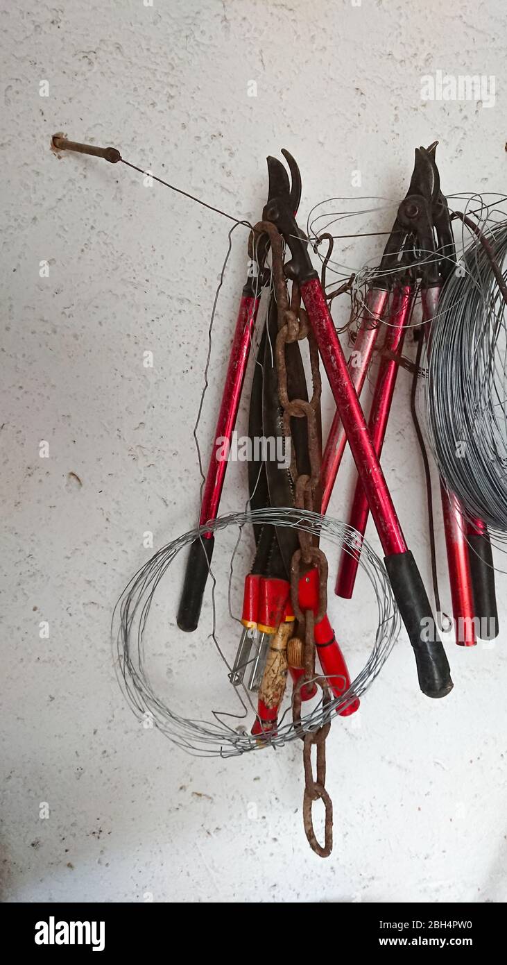 Cisailles, fils et autres outils de travail suspendus sur un mur blanc Banque D'Images