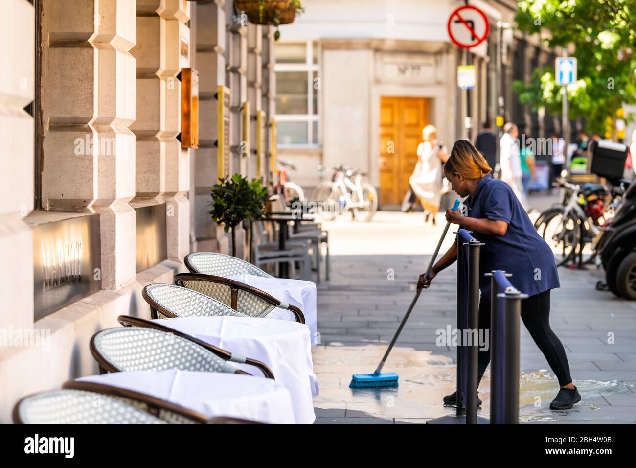 Londres, Royaume-Uni - 26 juin 2018 : une femme employée du restaurant un ouvrier nettoyant la rue au centre de la ville, en butant le sol humide pavé Banque D'Images