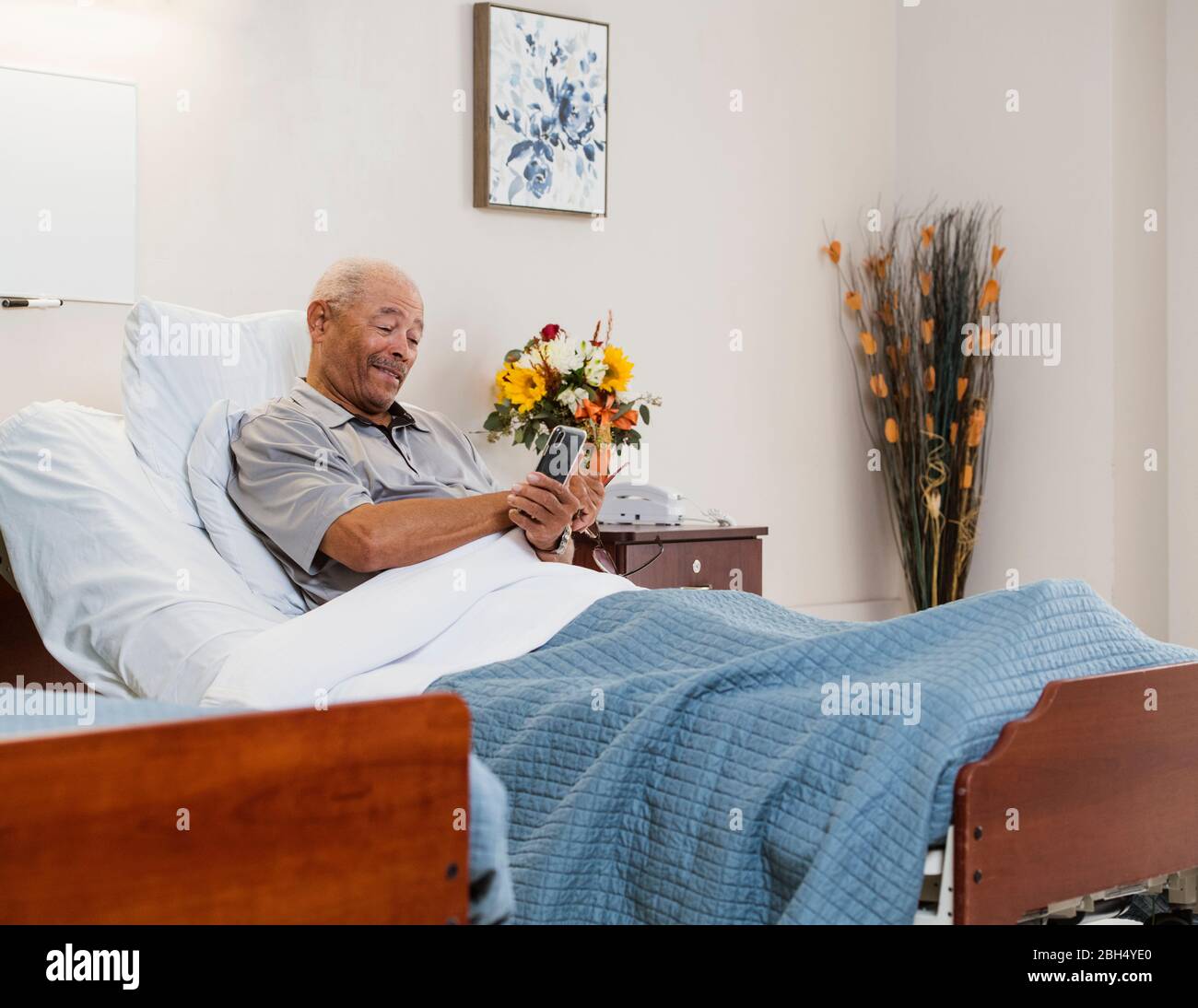 Homme senior tenant un smartphone et des fleurs dans le lit Banque D'Images