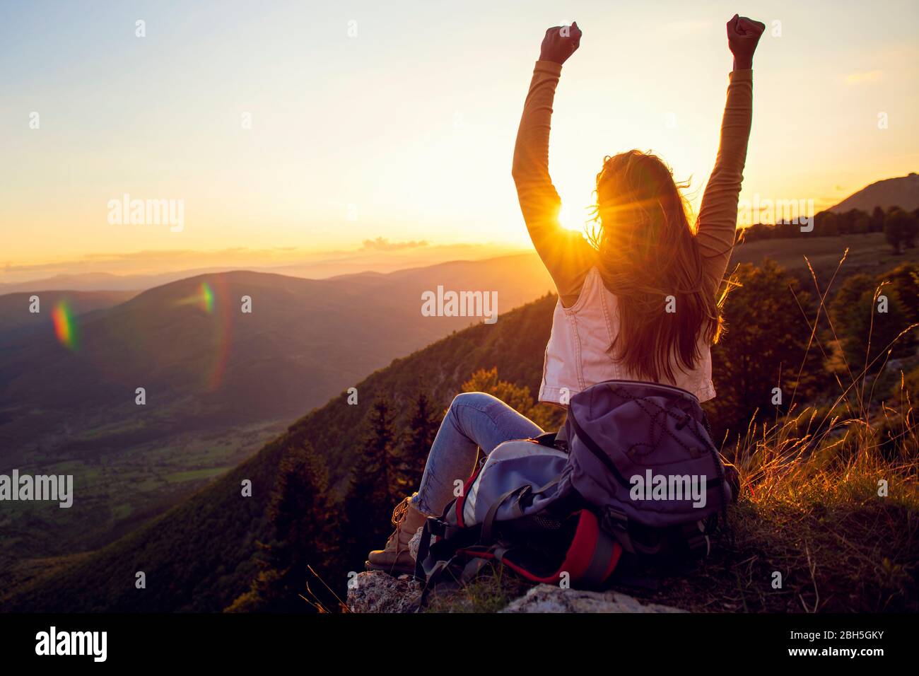 La jeune femme monte à la main sur le sommet de la montagne et coucher du soleil ciel fond abstrait. Banque D'Images