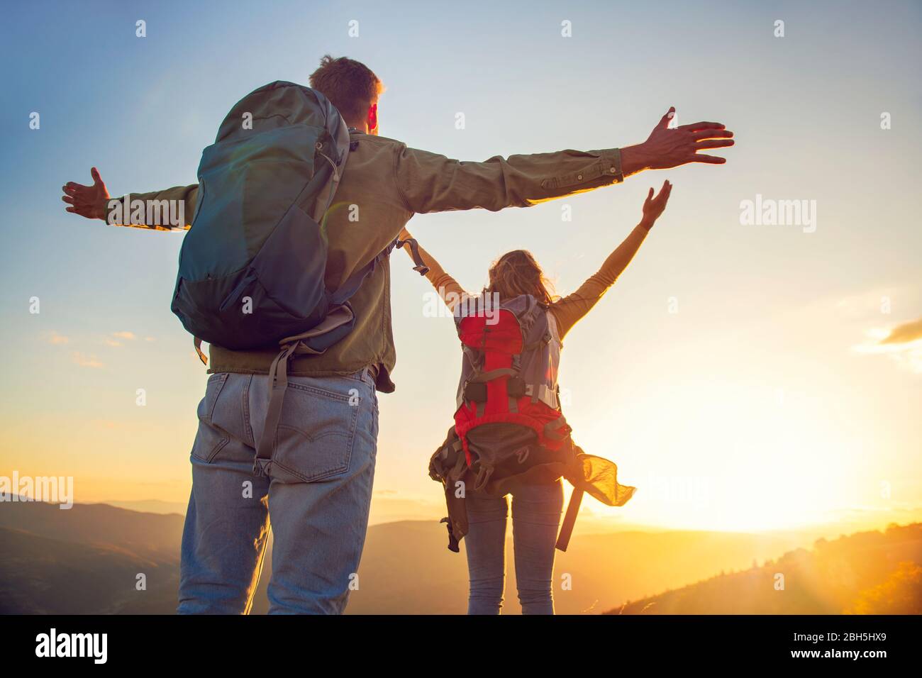 Couple avec bras levés tenant les mains et regardant le coucher du soleil Banque D'Images